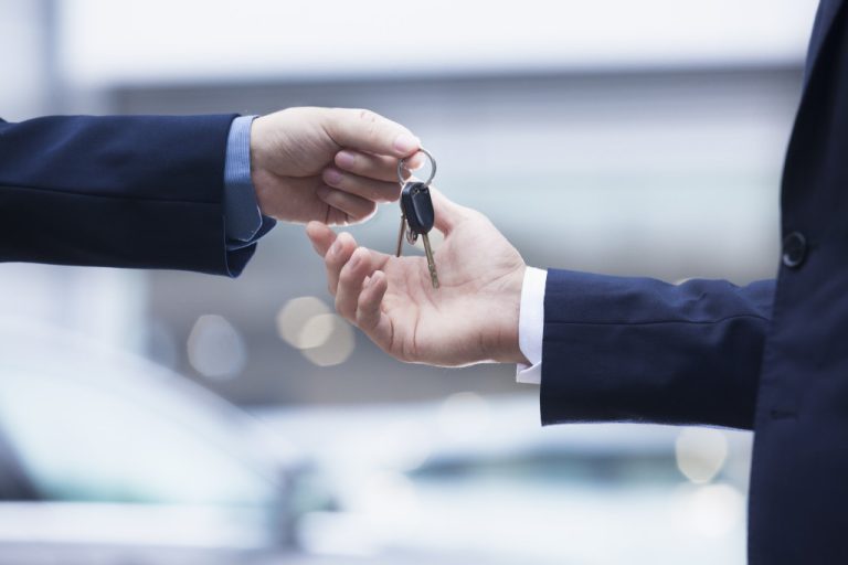 businessman handing car keys to another businessman outdoors